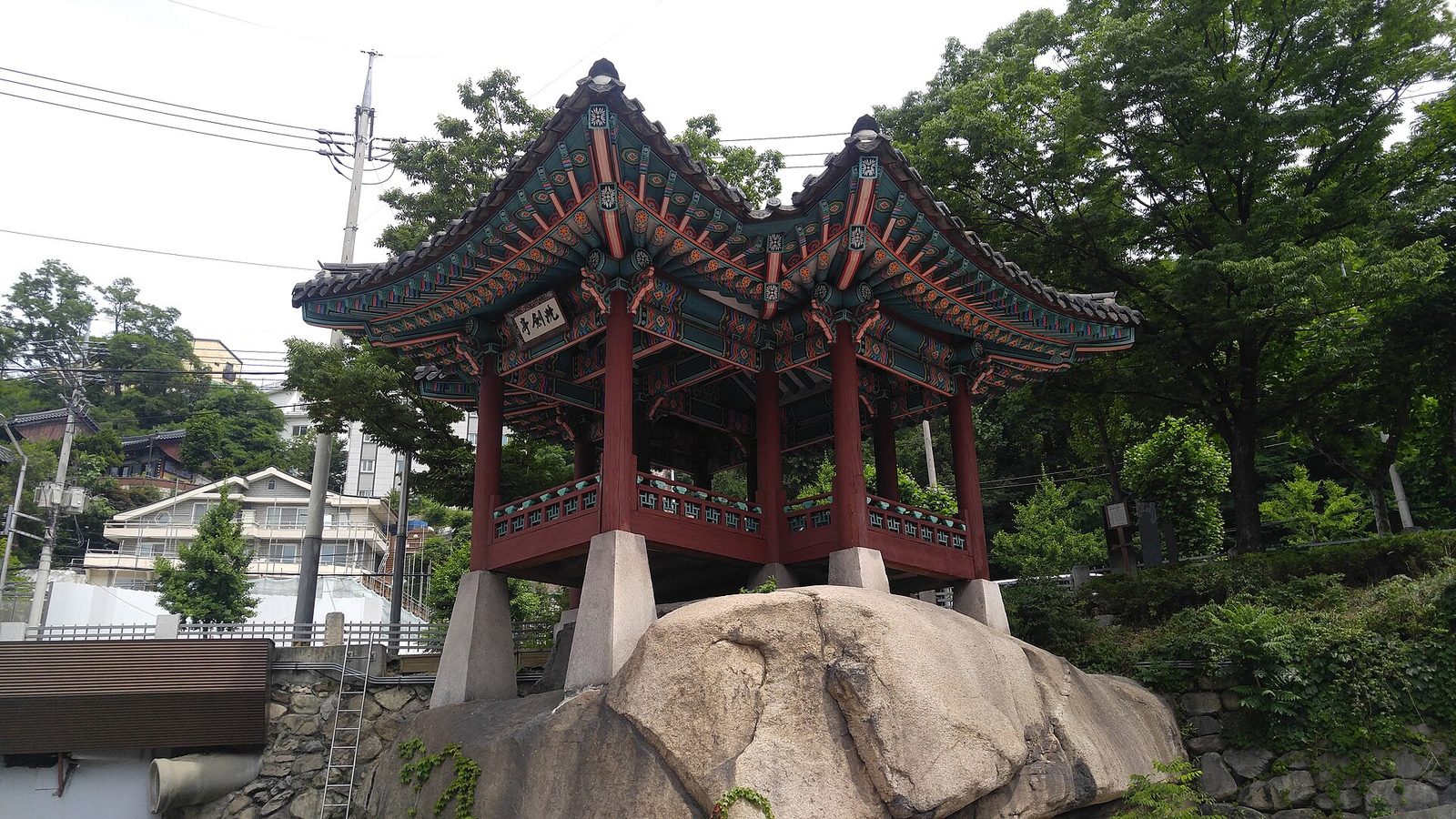 큰 바위 위에 올라앉은 세검정, 뒤로 마을 집들이 보이는 모습