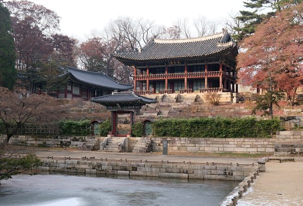 얼음이 낀 연못 너머 계단 위에 올라앉은 주합루, 붉은 단풍나무가 곁에 선 풍경