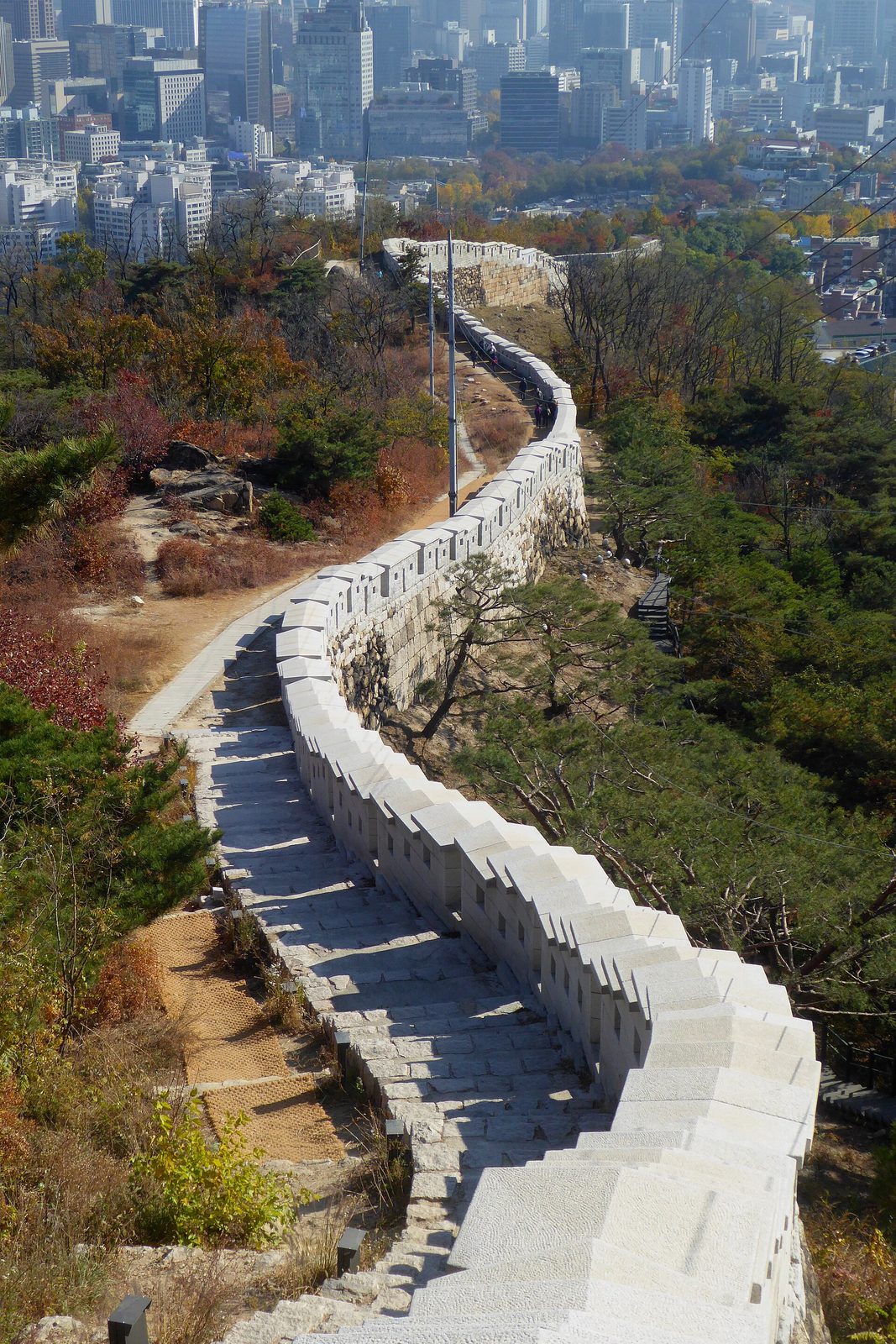 굽이굽이 이어지는 성벽 너머로 도심 빌딩이 보이는 성곽길